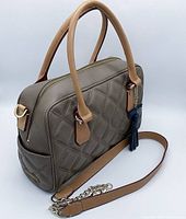 Angled front and side view of a beige quilted lambskin leather handbag showing handles, chain shoulder strap, zipper closure, and front pocket.