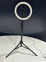 LED ring light attached on a black tripod stand with three legs, phone holder in the center of the ring, powered off