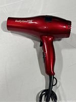 Side view of red BaByliss PRO Ceramix Xtreme hair dryer showing branding and handle with power button.