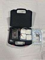 Closed black carrying case with digital NMES/TENS combo unit and accessories inside, showing electrode pads, wires and manual.
