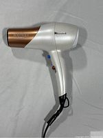 Side view of the silver and copper Conair Boutique hair dryer showing the brand name and cord attached.