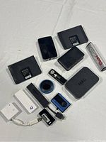 Photo showing all items in the lot arranged on a white cloth. Includes media players, battery pack, adapters, remote controls, and rechargeable battery.