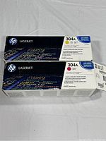 Photo of two HP LaserJet toner cartridges boxes, one yellow and one magenta, showing front and side details including product codes and descriptions.