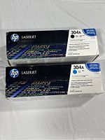 Front top view of two HP LaserJet toner cartridge boxes, one black and one cyan, showing model 304A on white color-coded labels.