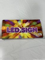 Colorful box with the words 'LED SIGN' in large purple letters on a multicolored background, showing packaging for the LED sign.