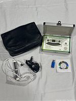 Quantum Resonance Magnetic Analyzer device with accessories including coiled cable with probe, USB flash drive, software CD, and black carrying case on white fabric background.