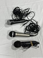 Photo shows three wired handheld microphones laid out on a white sheet, all with attached cables ending in 3.5mm jacks.