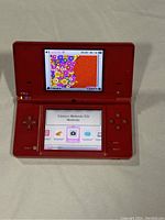 Red Nintendo DSi handheld console open showing both screens and controls.