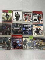 12 PlayStation 3 game cases laid out in 3 rows of 4, visible titles and cover art showing variety of games.