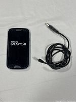 Front view Samsung Galaxy S3 Mini phone powered off with charging cable coiled beside it.