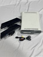 Xbox 360 Low Dashboard console and two Kinect sensors with AV cable laid out on white fabric.