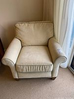 Front view of beige fabric armchair with cushioned seat and back, rounded arms, and solid wooden legs.