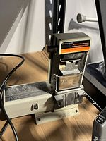 Front angle of the Black & Decker bench sander and sharpener, showing the sanding and sharpening section with branding and device structure.