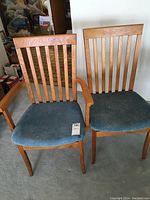 Two oak dining chairs side by side; one armchair and one side chair with blue upholstered seats, evidence of stains and cat hair on fabric.