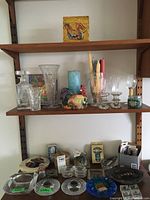 Shelf with crystal vases, ceramic rooster candle holder, candles, and napkin holder. Lower shelf shows ashtrays, coasters, and lighters.