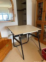 Photo of folding drafting table fully set up showing white angled surface and black metal legs.