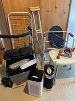 Lot showing walker, crutches, shower chair, air purifiers, and accessories arranged on floor with wood paneled background