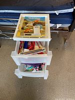 Full view of the three plastic bins stacked with the top bin holding knitting instruction booklets and knitting accessories inside lower bins