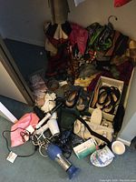 Photo showing assorted scarves, belts, purses, shoes, and small appliances such as hairdryers and curling iron on carpeted floor