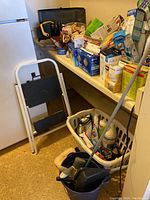 Photo of table containing toolbox, multiple boxes of light bulbs, cleaning products, step stool, and laundry basket with various items.