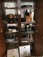 Full pantry view showing copper fondue pot on top shelf, wooden knife block with 2 Henckels knives, white electric knife sharpener, electric hand wand mixer, bakeware, linens and other kitchen items spread on shelves.