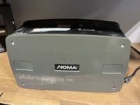 Front and top angled view of the NOMA Backup Power System 1800 showing brand logo and model designation on the gray front panel with ventilation slots.