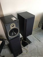 Two B&W speakers placed on Atlantis stands on carpeted floor
