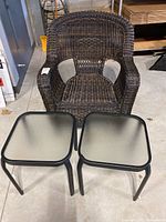 Front view of dark brown faux wicker armchair with two small square glass top tables placed in front.