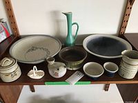 Full overview of the pottery collection showing all bowls, jug, creamer, and other ceramic pieces on shelf.