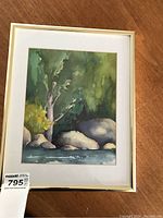 Framed watercolour artwork showing trees, rocks, and water scene.