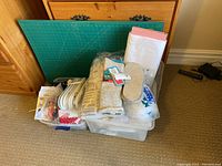 Lot overview showing green cutting mat, plastic bins filled with various sewing fabrics, fiber fill, and accessories.