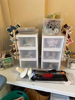 Photo showing two wooden thread racks filled with colorful spools, two white plastic drawer units, and sewing tools like scissors and spool holders on table.