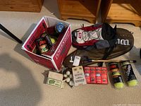 Wide view of entire sports lot showing open box filled with multiple tennis ball cans, loose ping pong balls and their packaging, Hsingta bike pedals in box, Wilson tennis racket cover.