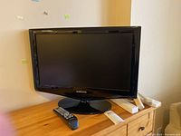 Samsung 21-inch TV on wooden table with remote and power bars.