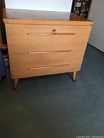 Front angled view of cedar chest showing overall form, recessed handle grooves, and keyhole on hinged lid.