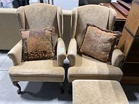 Two beige wingback chairs with throw pillows
