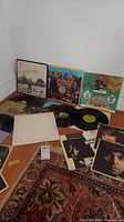 Photo showing seven vinyl records with sleeves spread on floor including Sgt. Pepper's, Abbey Road, White Album, and All Things Must Pass. Various inserts and photo cutouts visible.