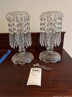 Photo showing two matching glass candle holders with hanging glass prisms and detached glass pieces on a wooden surface.