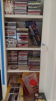 Photo showing a shelf with a wide selection of CD jewel cases neatly stacked and some loose in the bottom storage bin.