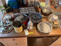 Wide view of all items including cookie cutters, bundt pan, pie plates, flour sifter, and other bakeware on table.
