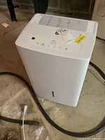 White GE dehumidifier with hose on concrete floor, showing top and side views.