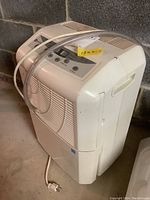 Maytag dehumidifier unit in a basement with power cord coiled on top.
