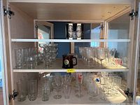 Wide view showing multiple shelves of assorted clear glass drinking glasses, dessert dishes, bowls, and some goblets.