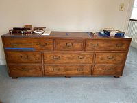 Front view of the wooden dresser with nine drawers and brass handles, showing clear wood grain and rectangular shape.