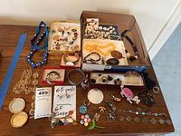 Overall view of assorted jewelry laid out on table including necklaces, bracelets, pins, earrings, rings in mixed materials.
