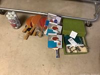Overview of paddles, both used and new in packaging, ping pong balls in container, and boxed net set