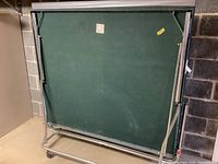 Photo of the folded green ping pong table showing its playing surface and metal frame on wheels.