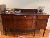 Full front view of wooden sideboard with various glass and metal items on top