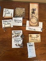 Overview of all jewelry items including pocket blades labeled 10K on 'U' clasp, sterling pocket blade, sterling compact, bracelets, earrings on display board, Napier earrings and price tag