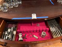 Drawer of sterling silver flatware and utensils in a wooden chest showing knives, forks, spoons, and salt and pepper grinder.